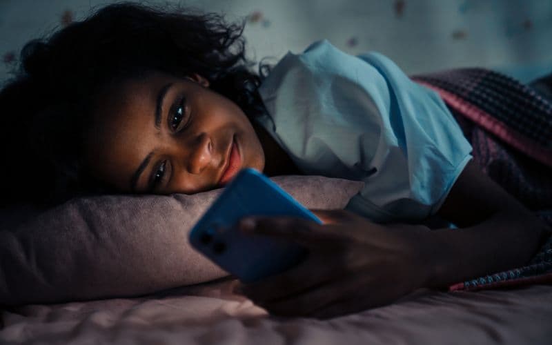 mujer en una cama viendo celular